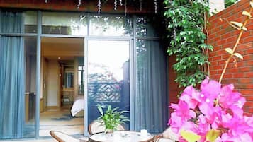 A room with a large sliding glass door leading to a balcony, a round table with chairs, and a potted plant.