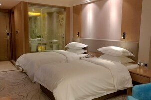 Habitación de hotel con una cama grande, una mesita de noche, un espejo y una zona de ducha con mampara de cristal.