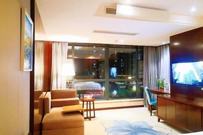 A hotel room with a large window, a bed, a TV, a sofa, and a small table. - Century Chanson Hotel (Mianyang)