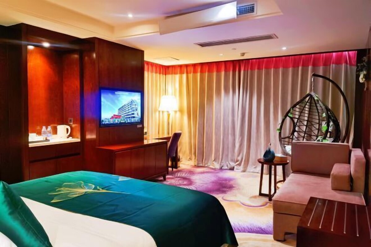 A hotel room with a bed, a TV, a desk, a chair, a sofa, and a hanging chair.