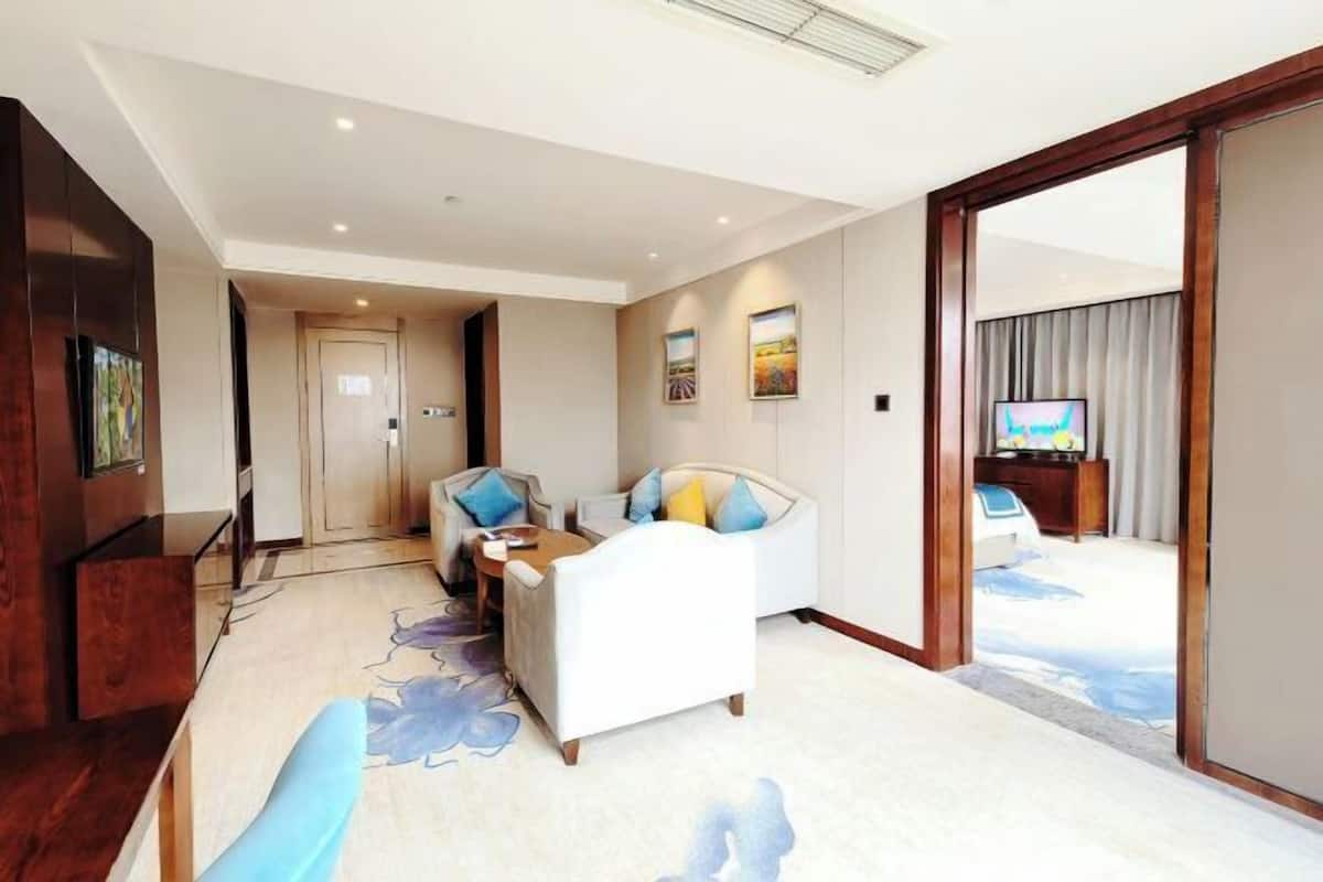 A hotel room with a sofa, a small table, a TV, and a view of the outside.