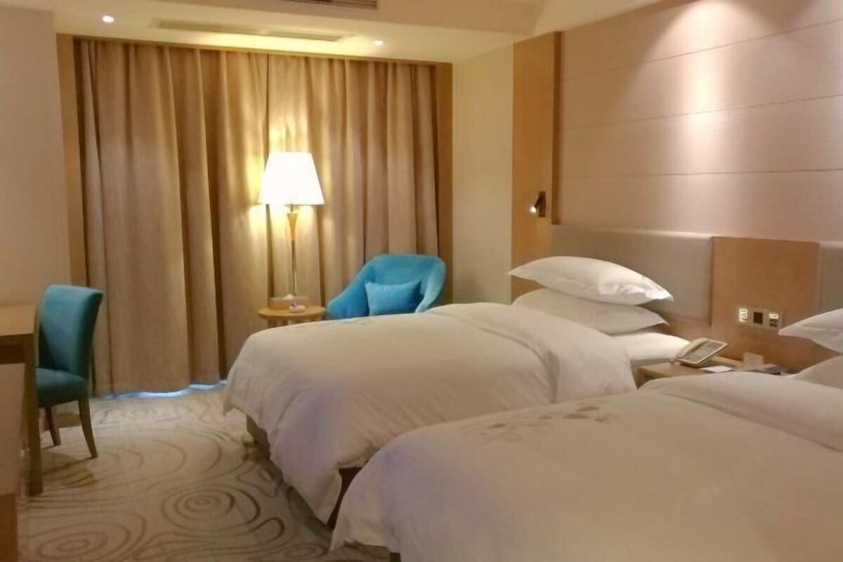 A hotel room with two beds, a desk, a chair, a lamp, and a phone on the nightstand.