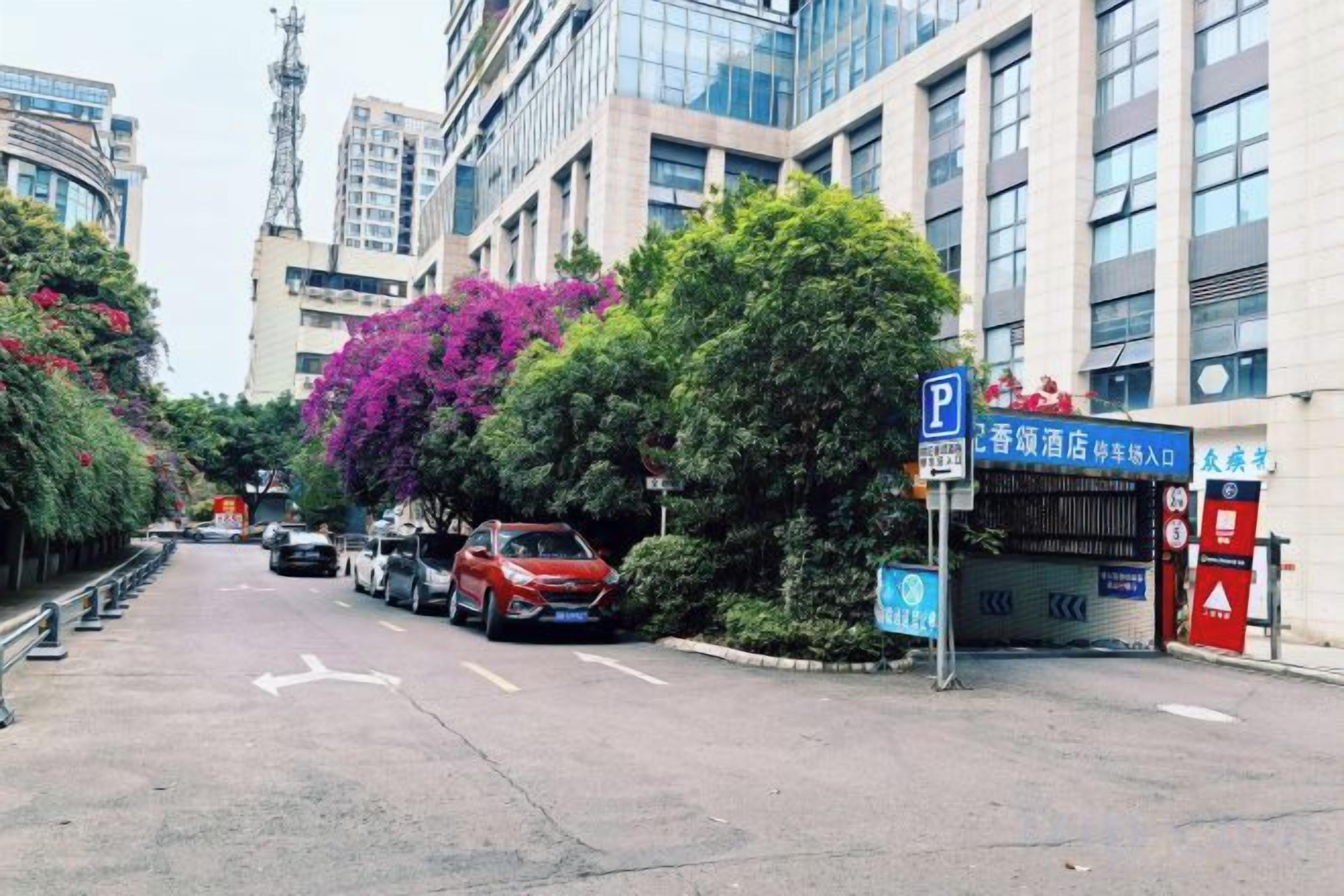 A street view with parked cars, a parking sign, and a building with a blue sign.