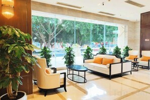 A hotel lobby with a sofa, armchairs, a coffee table, and a large window offering a view of the street. - Century Chanson Hotel (Mianyang)
