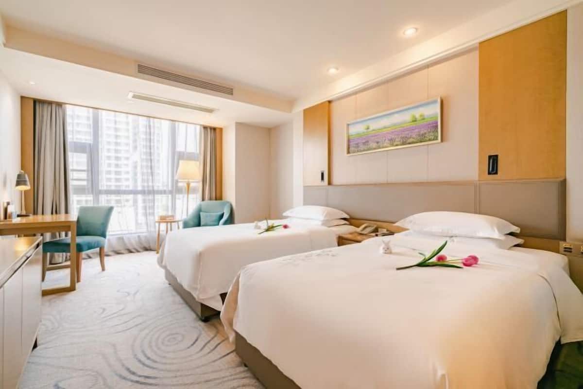 A hotel room with two beds, a desk, a chair, and a painting on the wall.
