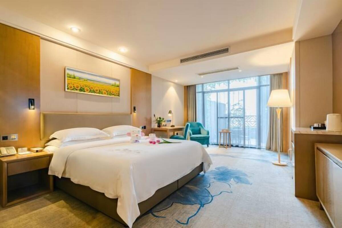 A hotel room with a large bed, bedside tables, a desk, a chair, and a window with curtains.
