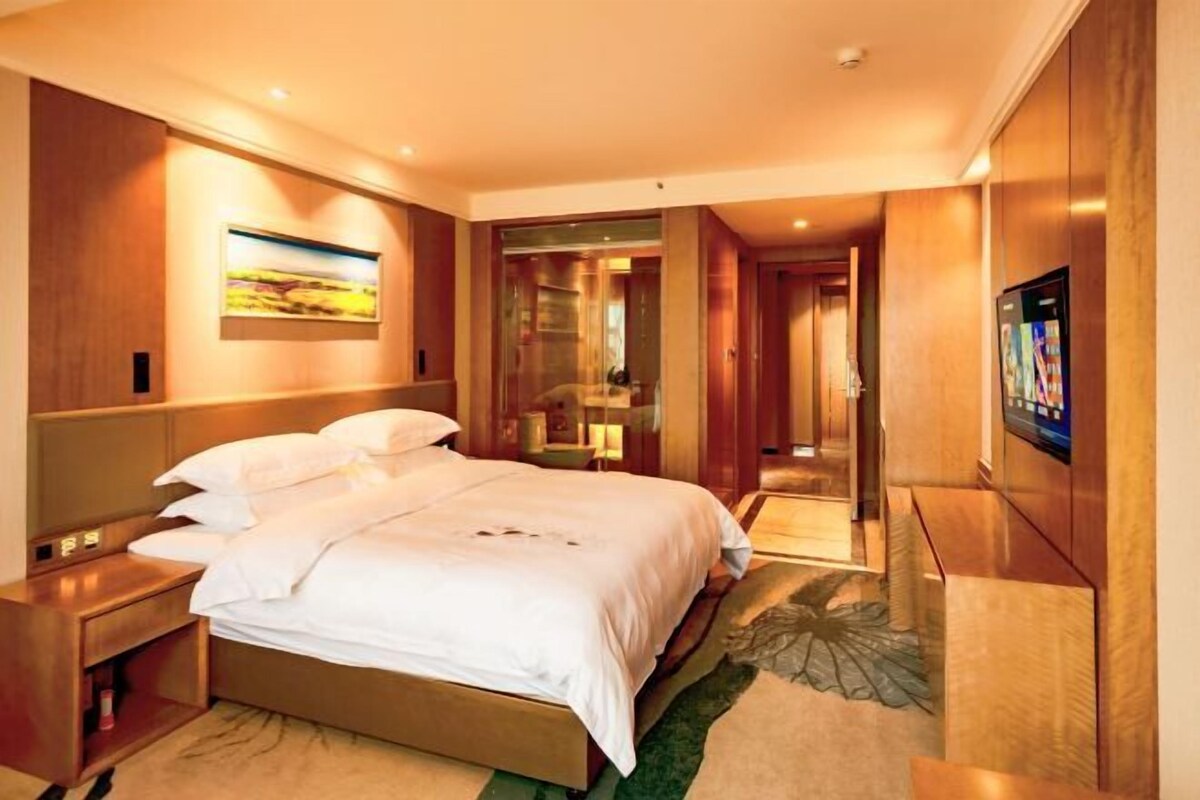 A hotel room with a large bed, a TV mounted on the wall, and a painting on the wall.