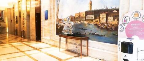 A hotel lobby with a large painting of a canal scene, a marble floor, and a table with a small statue.