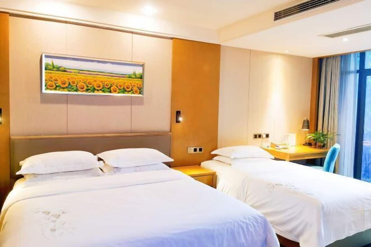 A hotel room with two beds, a desk, a chair, and a painting on the wall.