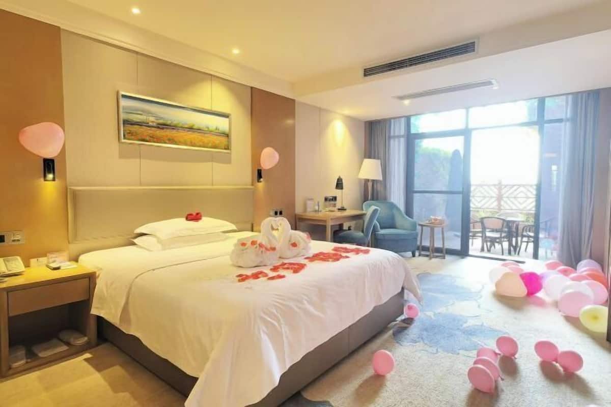 A hotel room with a bed, a desk, a chair, and a balcony with balloons.