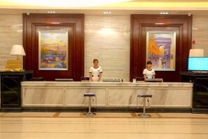 A reception desk with two staff members, framed artwork on the walls, and a television on the right. - Century Chanson Hotel (Mianyang)