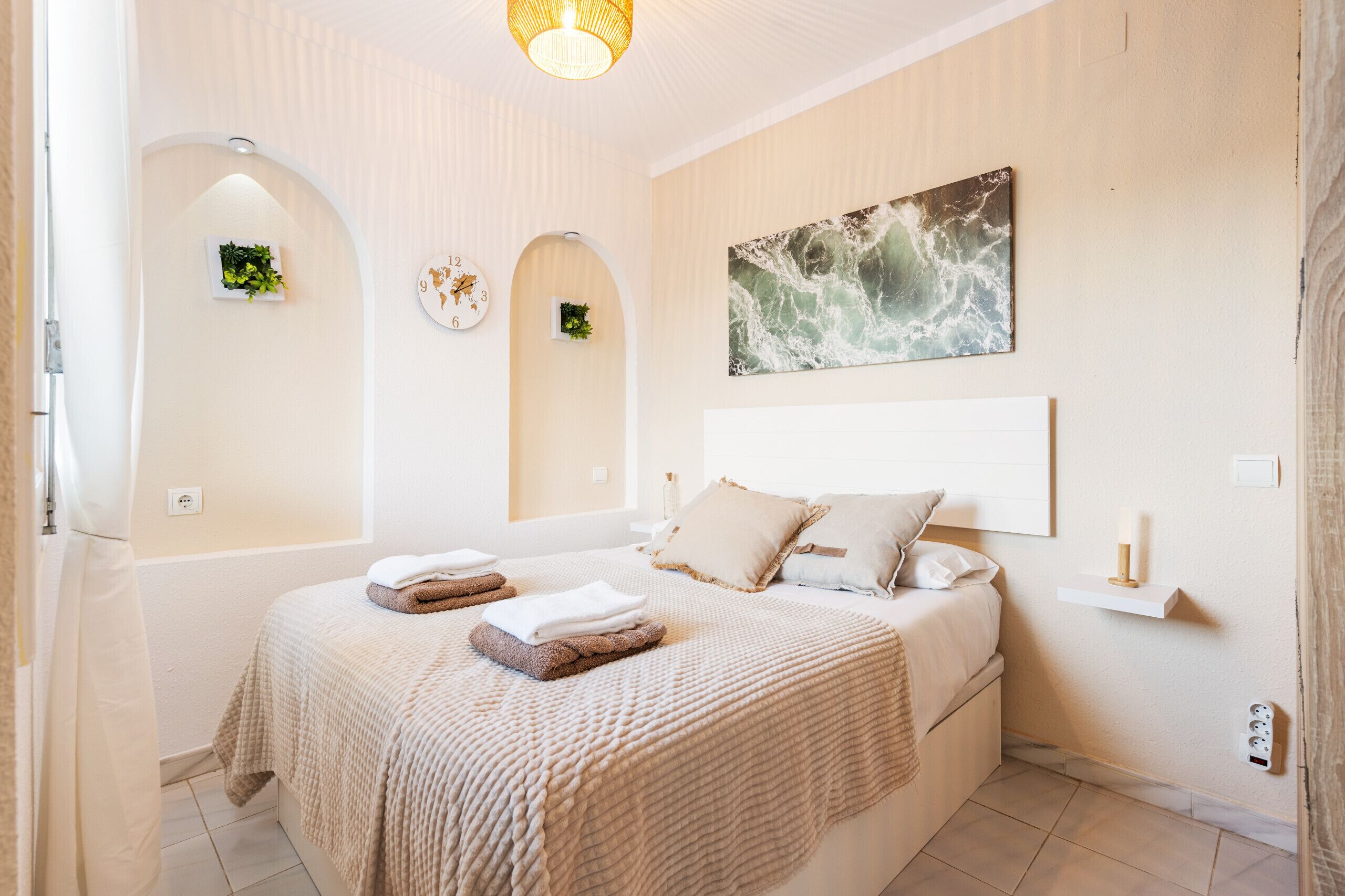 A bedroom with a large bed, a wall clock, a painting, and a small shelf.