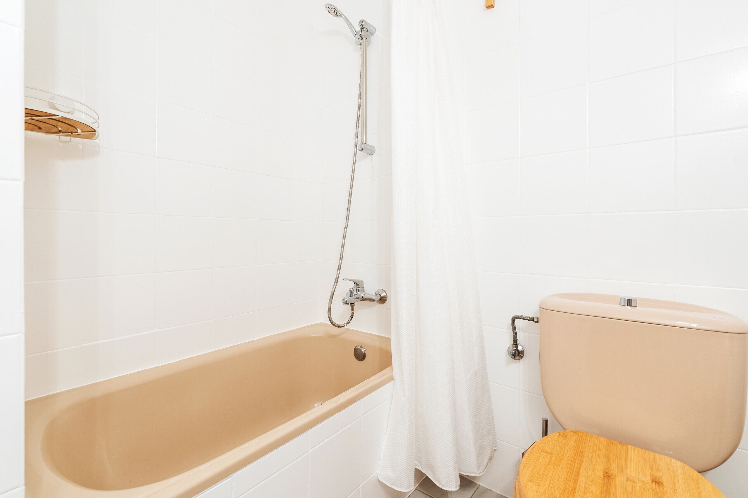 Un baño con una bañera color beige, un inodoro y un cabezal de ducha.