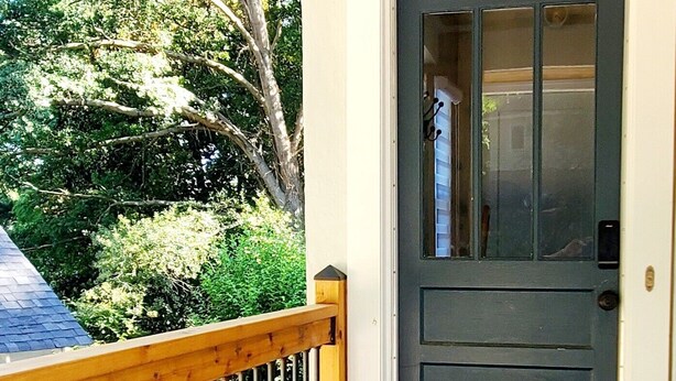 A front door with a dark-colored door and a wooden railing. - Modern Comfort in Downtown Greenville 4br 2ba (Greenville)