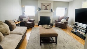 A living room with a fireplace, two armchairs, a sofa, a coffee table, and a television. - Modern Comfort in Downtown Greenville 4br 2ba (Greenville)