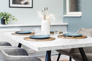A dining table with blue plates, white pitcher, and glassware, set on woven placemats.