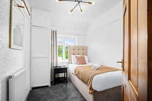 A bedroom with a bed, a nightstand, a radiator, a window, and a door.