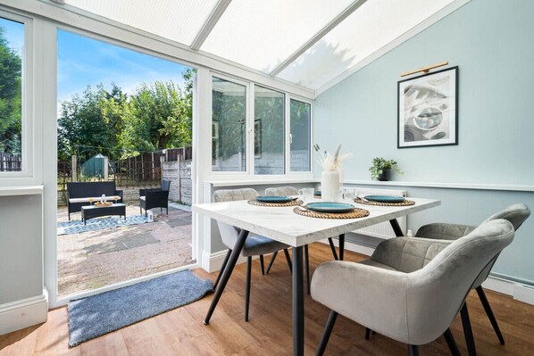 A conservatory with a dining table set for four, surrounded by chairs.