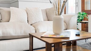 A living room with a beige sofa, a wooden coffee table, and a potted plant. - The unit comes high-speed WiFi, hotel-quality linen, and toiletries for your comfort. (Birmingham)