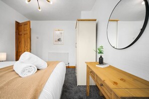 A hotel room with a bed, a wooden nightstand, a mirror, a radiator, and a door.