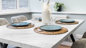A dining table set with blue plates, clear glasses, and a white vase with dried plants. - The unit comes high-speed WiFi, hotel-quality linen, and toiletries for your comfort. (Birmingham)