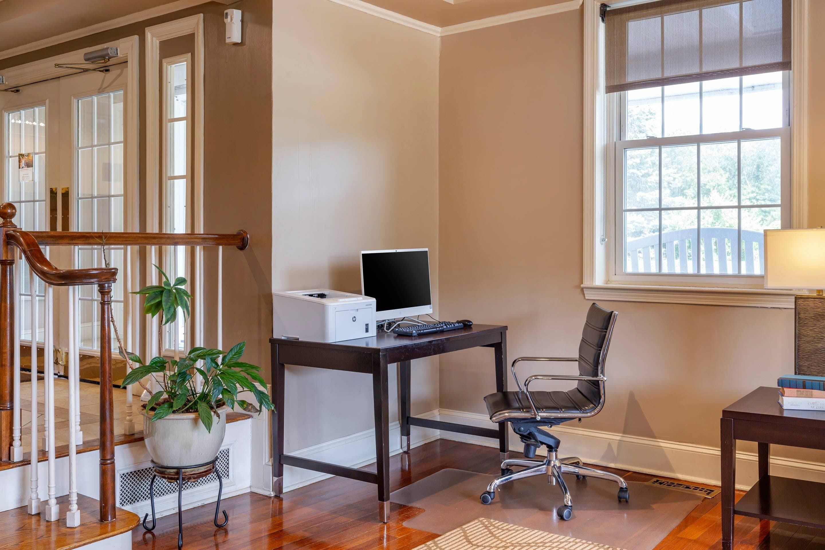 A home office with a desk, computer, chair, and a staircase with a plant.