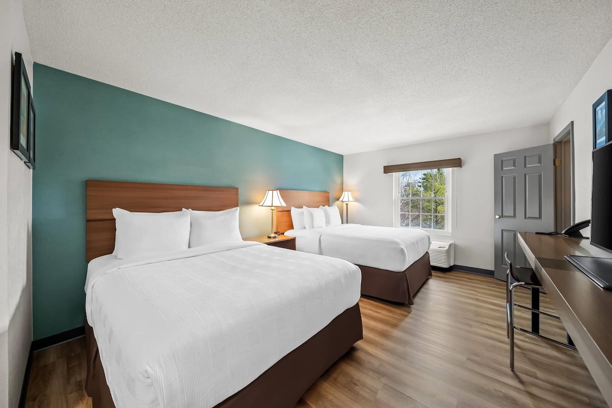 A hotel room with two beds, a desk, and a TV.