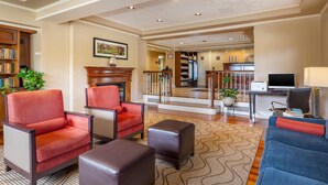 A spacious living area with a fireplace, bookshelves, a television, and a staircase leading to an upper level. - MainStay Suites Foxboro – Mansfield (Foxborough)
