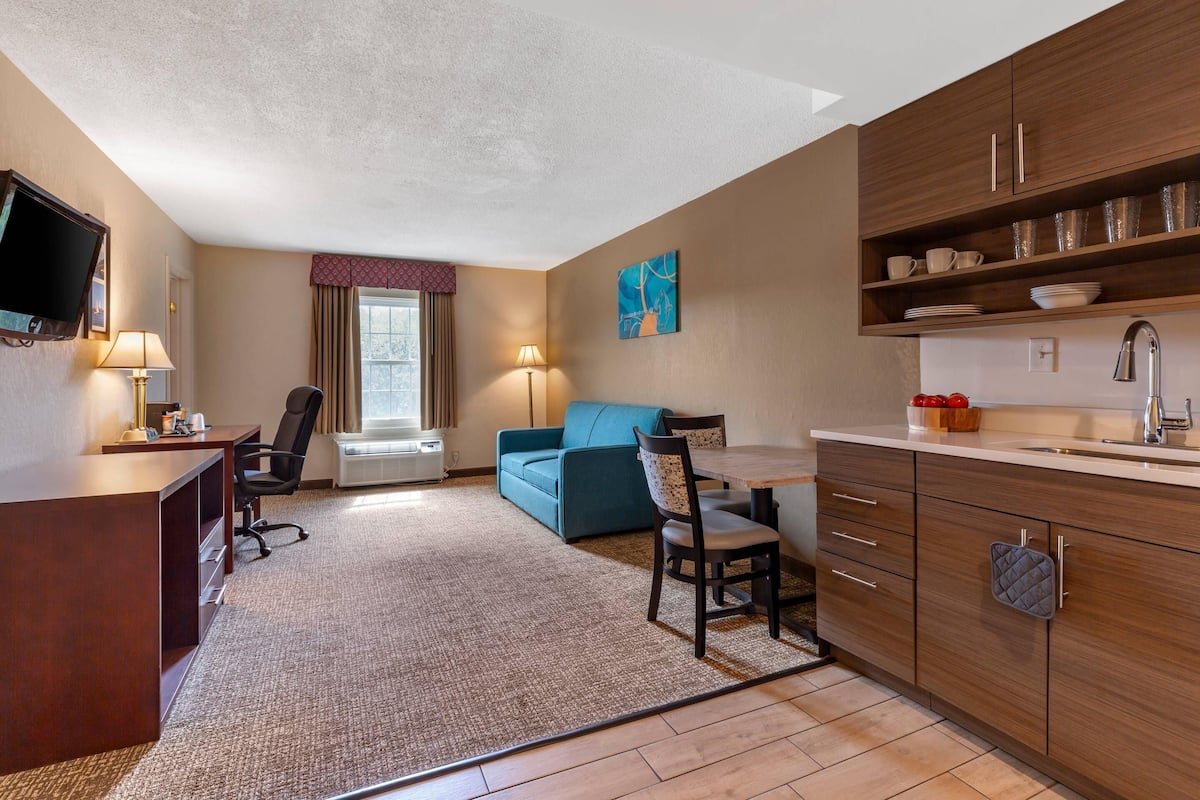 A hotel room with a kitchenette, a sofa, a dining table, and a TV.