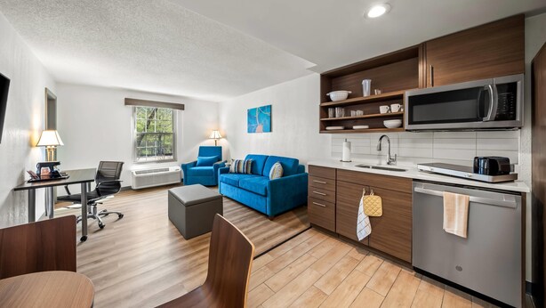 A modern living room with a sofa, a dining table, and a kitchen area with a microwave and dishwasher. - MainStay Suites Foxboro – Mansfield (Foxborough)