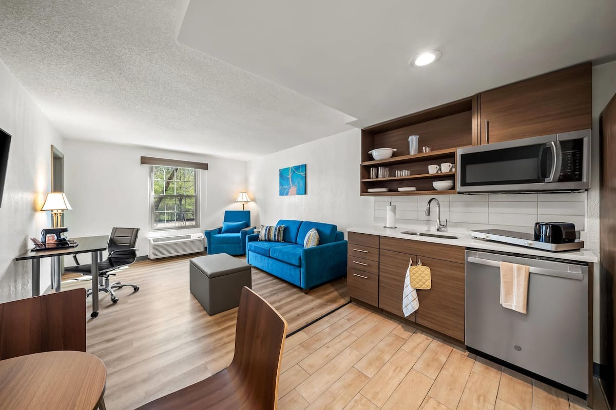 A modern living room with a sofa, a dining table, and a kitchen area with a microwave and dishwasher.