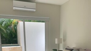 A bedroom with a large bed, a nightstand, a lamp, and a sliding glass door leading to a balcony with a view of greenery. - Punta Cana 2BR apt with private jacuzzi (Punta Cana)
