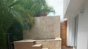 A patio area with a table, wicker chairs, a decorative urn, and a stone wall with steps. - Punta Cana 2BR apt with private jacuzzi (Punta Cana)