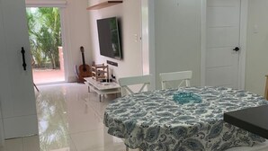 A dining area with a table and chairs, a television mounted on the wall, and a guitar in the background. - Punta Cana 2BR apt with private jacuzzi (Punta Cana)