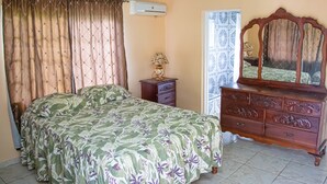 A bedroom with a bed, a dresser, a mirror, and an air conditioning unit. - Charlie's Cottages (Negril)