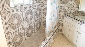 A bathroom with ornate tiled walls, a shower curtain with a floral pattern, and white cabinets with gold handles. - Charlie's Cottages (Negril)