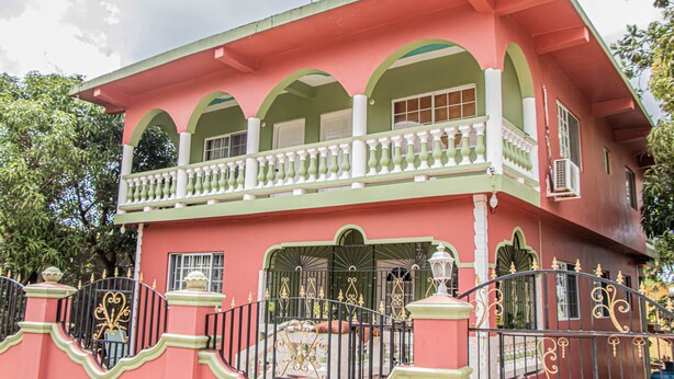 A two-story building with a balcony, arched windows, and a gated entrance. - Charlie's Cottages (Negril)