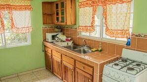 A kitchen with wooden cabinets, a gas stove, and a window with curtains. - Charlie's Cottages (Negril)