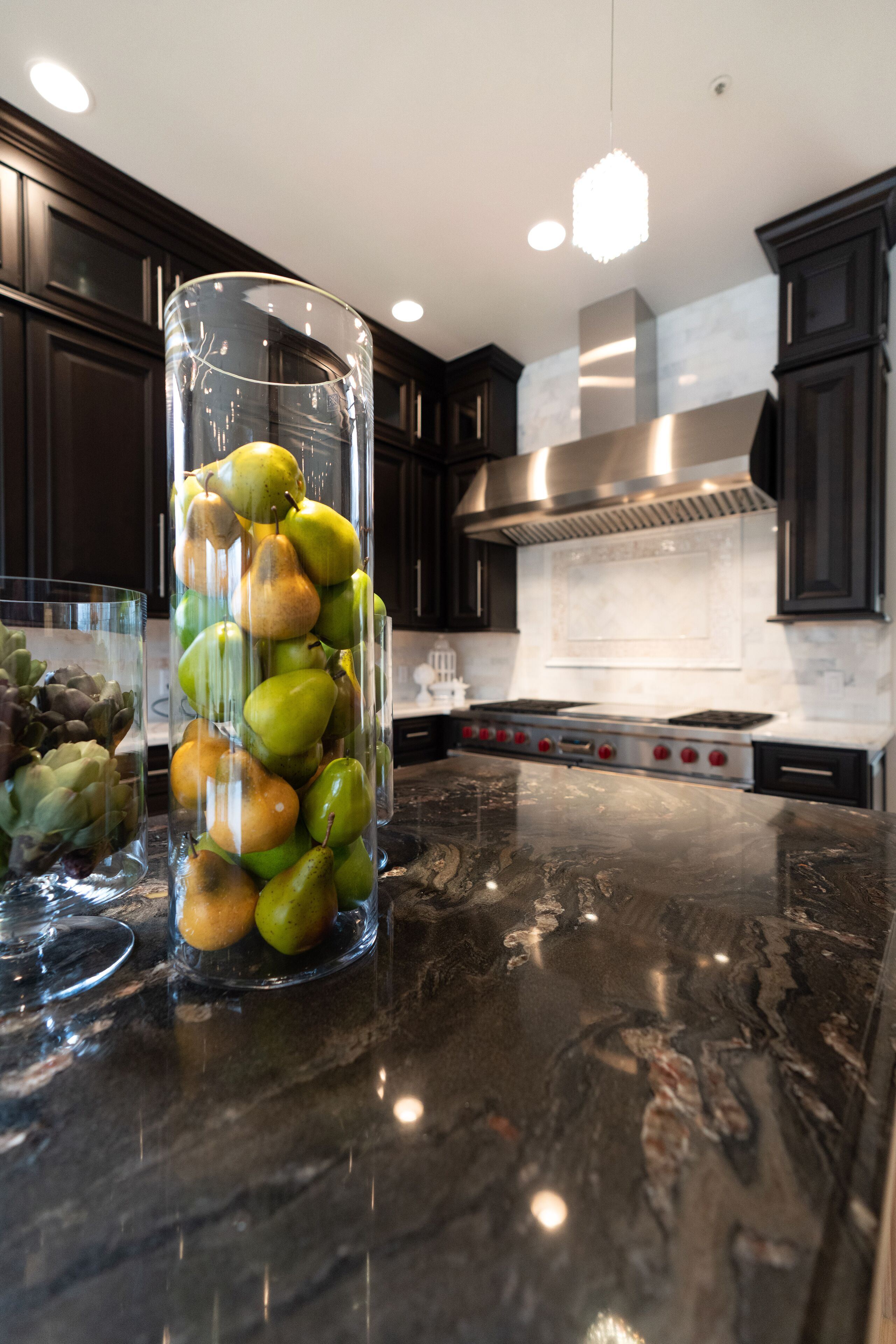 A kitchen with dark wooden cabinets, a stainless steel range hood, and a marble countertop.