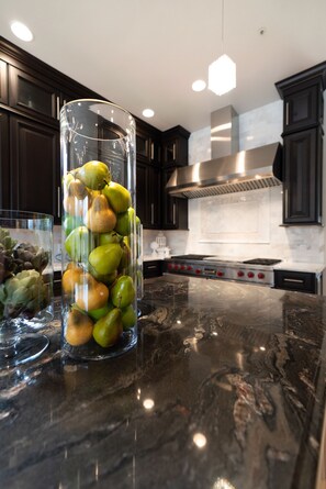 A kitchen with dark wooden cabinets, a stainless steel range hood, and a marble countertop. - Uncommon Grounds Estate (Dallas)