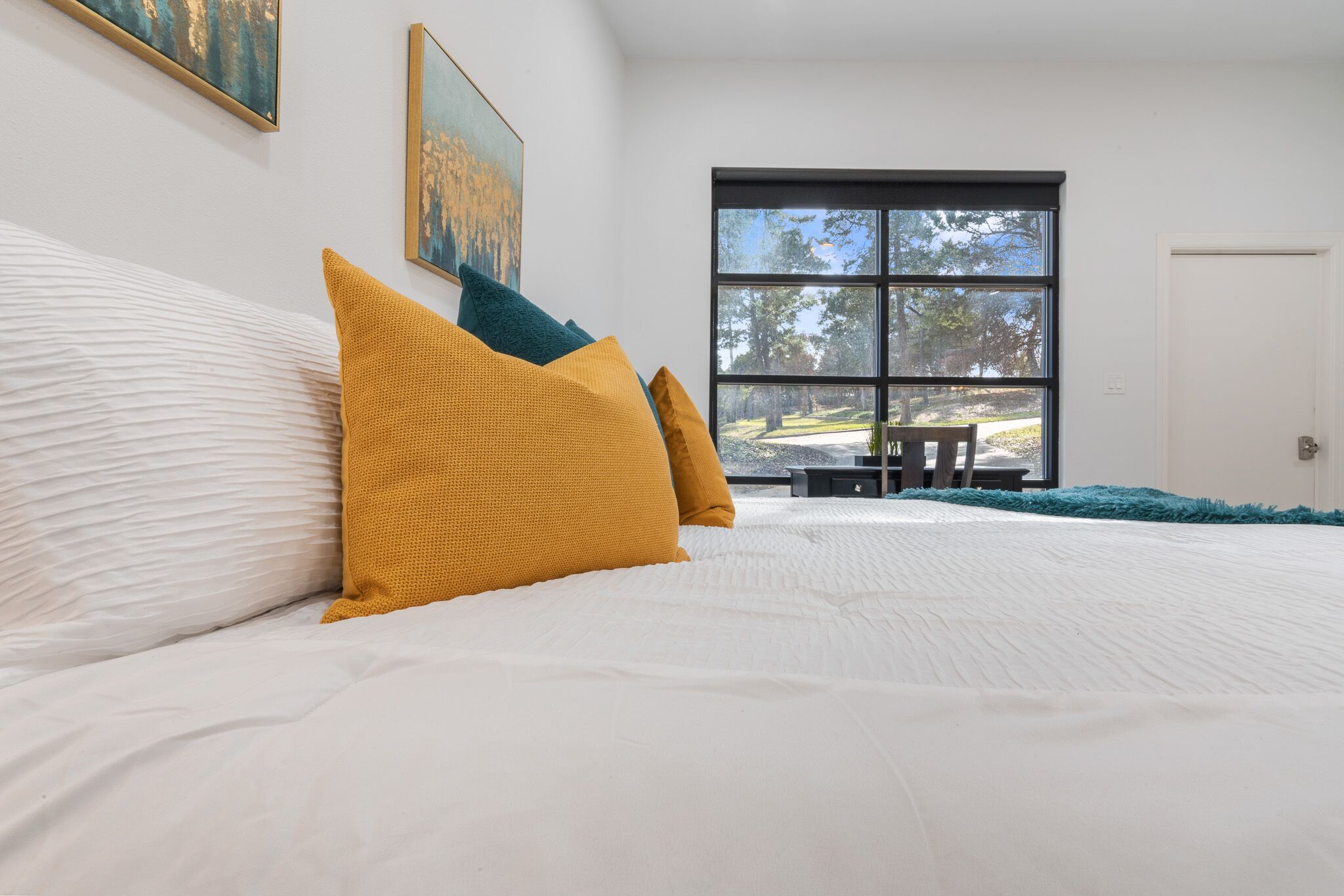 A bedroom with a large bed, white bedding, and a view of a park through a large window.
