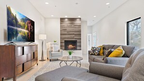 Ein modernes Wohnzimmer mit Flachbildfernseher, Kamin, grauen Sofas und einem Couchtisch.