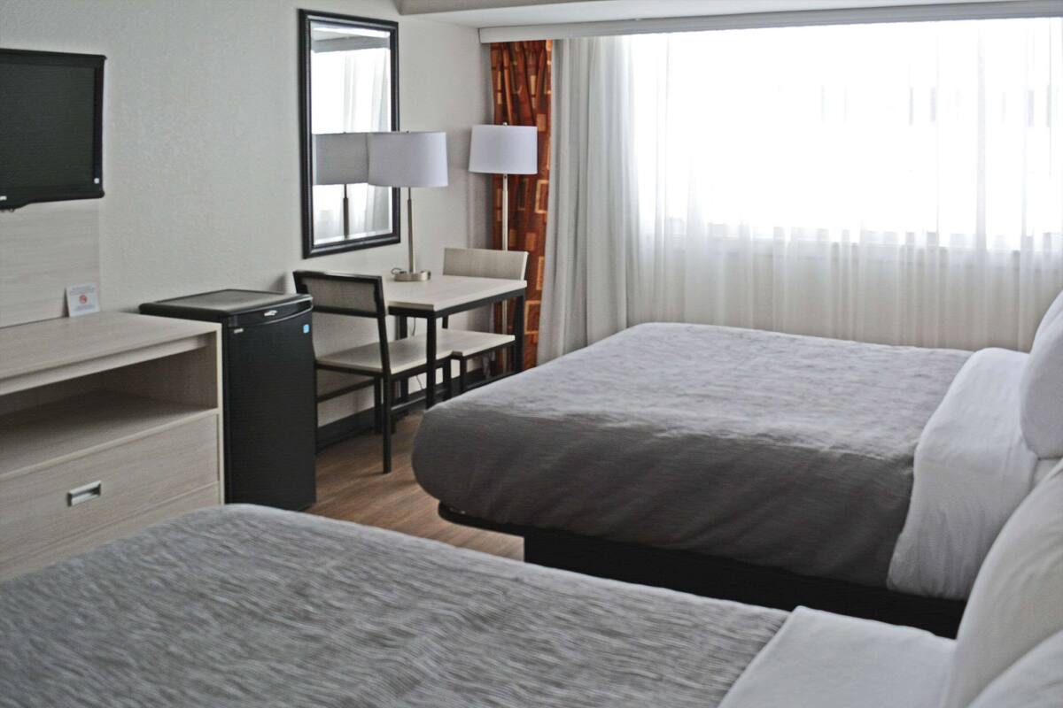 Quarto de hotel com duas camas, uma escrivaninha, uma cadeira, uma televisão e uma janela com cortinas.