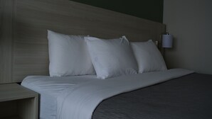 A neatly made bed with white bedding and a grey blanket, a wooden headboard, and a bedside table with a lamp. - Quality Inn & Suites Syracuse - Carrier Circle (East Syracuse)