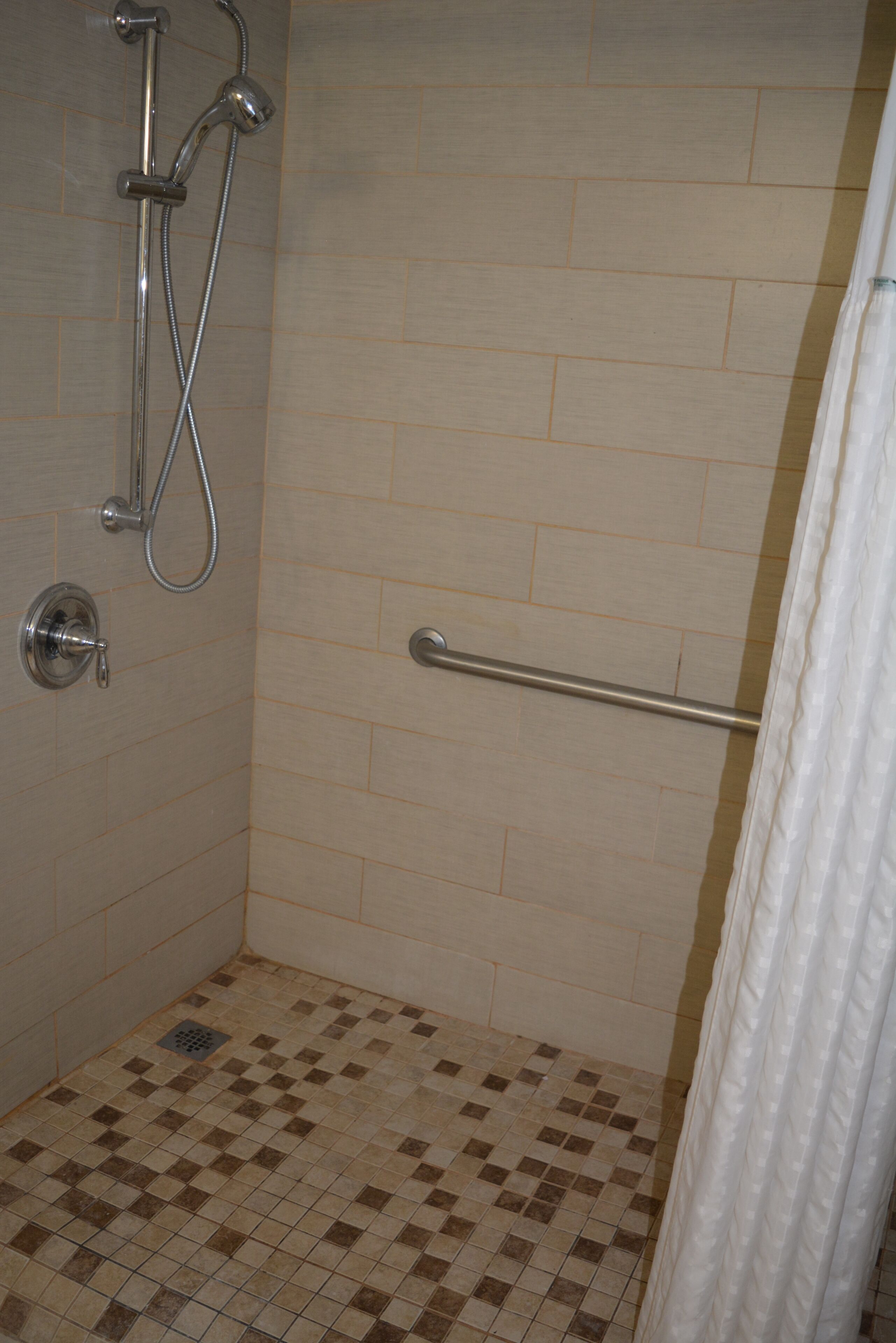 A shower with a grab bar, tiled walls, and a checkered floor.