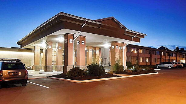 A hotel with a covered outdoor area, multiple columns, and a parking lot with several cars. - Quality Inn & Suites Syracuse - Carrier Circle (East Syracuse)