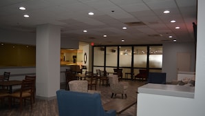 A spacious indoor area with multiple seating arrangements, including tables and chairs, and a reception desk. - Quality Inn & Suites Syracuse - Carrier Circle (East Syracuse)