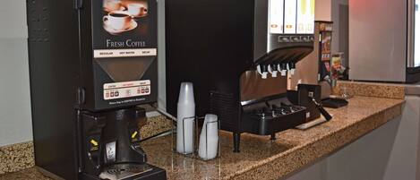 Two coffee machines on a granite countertop with a kitchen area in the background.