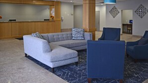 A lobby with a reception desk, a grey sectional sofa, and blue armchairs. - Quality Inn & Suites Syracuse - Carrier Circle (East Syracuse)