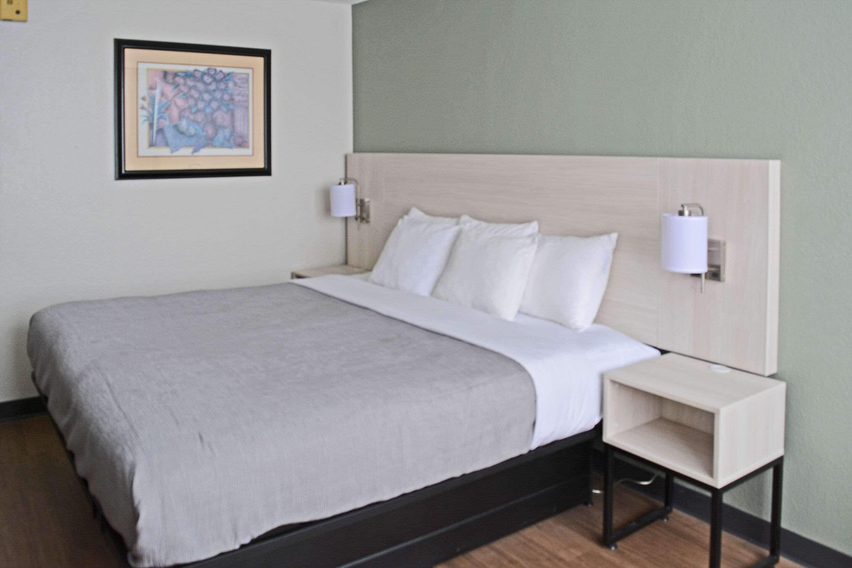 A neatly made bed with white linens, a headboard with integrated wall sconces, and a small bedside table.
